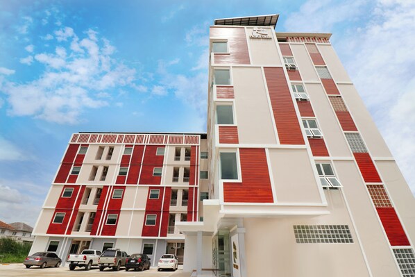 A multi-story hotel with a modern design, featuring a combination of red and white exterior panels, multiple balconies, and a parking area with several vehicles. - Triple Trees (Lam Luk Ka)