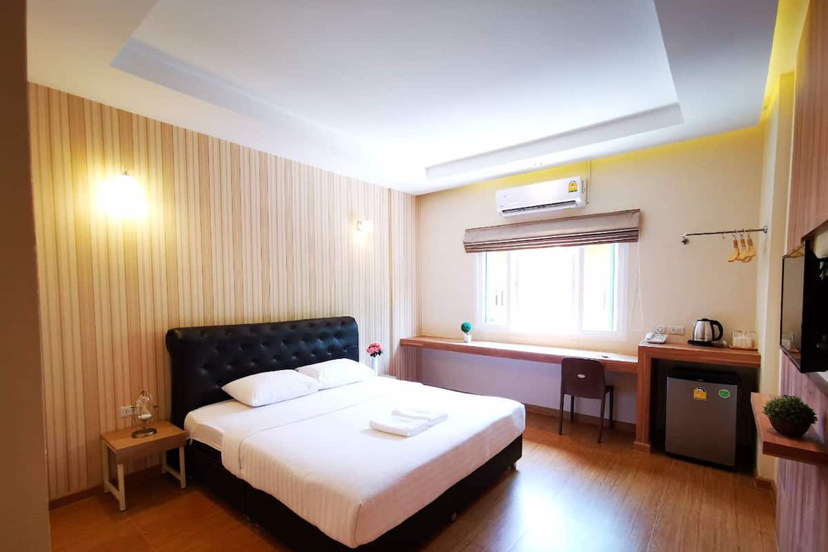 A hotel room with a bed, bedside table, desk, chair, and a small kitchenette.