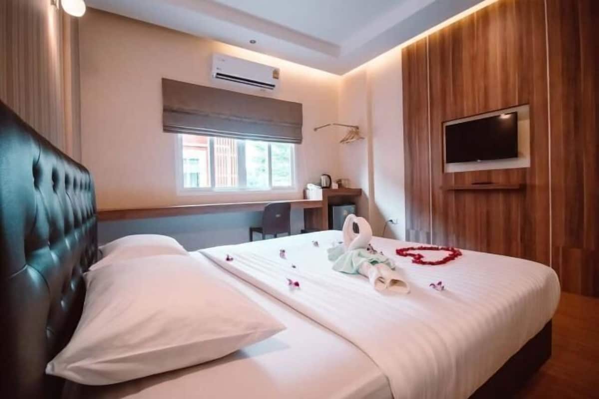 A hotel room with a bed, a TV, an air conditioning unit, a window, and a desk.