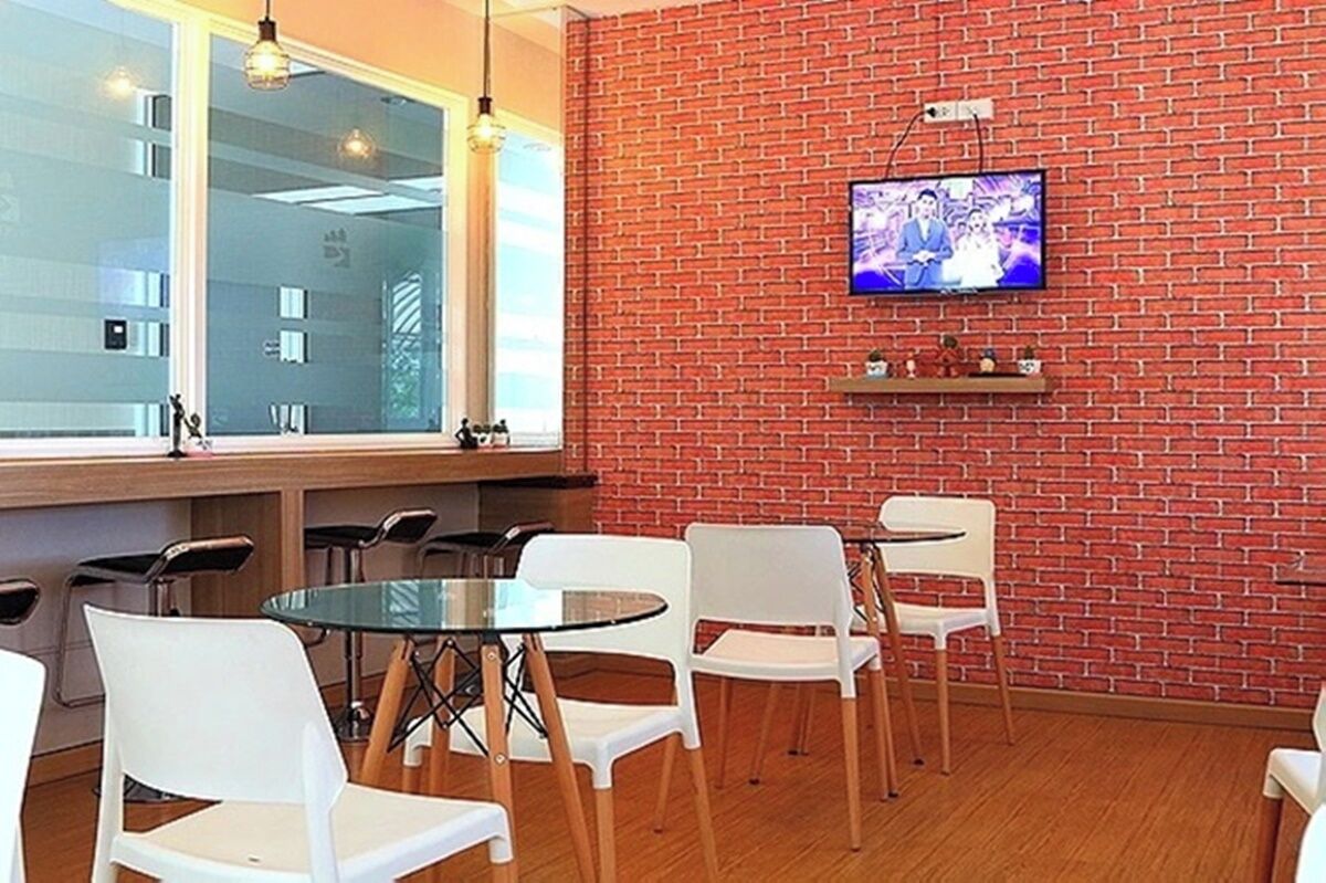 A modern room with a brick wall, a television mounted on it, and a glass table with white chairs.