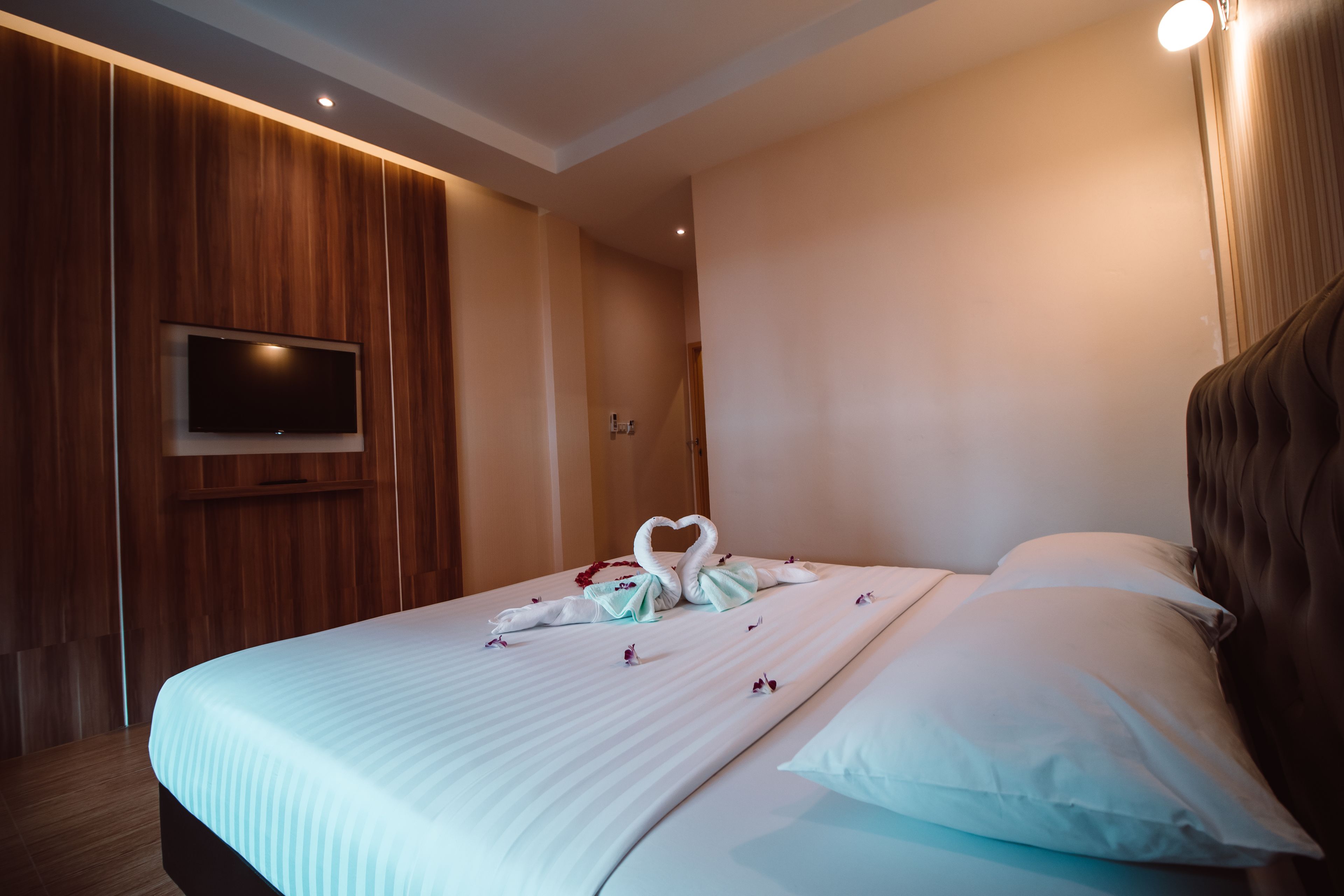Habitación de hotel con cama, televisor de pantalla plana en la pared y un diseño de paneles de madera en el lado izquierdo.