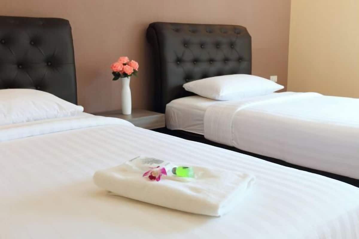 A hotel room with two beds, a nightstand with a vase of flowers, and a neatly folded towel on the bed.