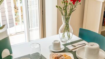 Uma mesa posta com pratos, chávenas, um vaso de flores e croissants.