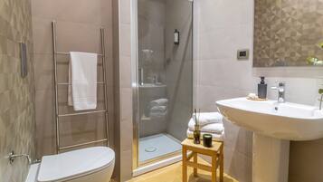 A modern bathroom with a glass-enclosed shower, a white toilet, and a sink with a wooden stool.