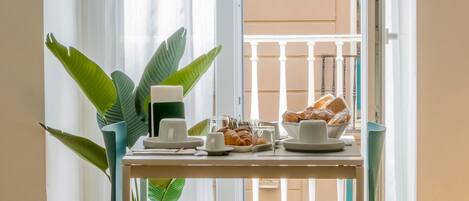 A dining area with a table set for two, a potted plant, and a view of a balcony with a railing.