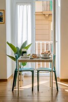 Zona pranzo con tavolo apparecchiato per due persone, una pianta in vaso e vista su un balcone con ringhiera.
