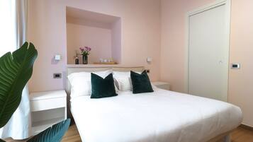 A bedroom with a bed, nightstands, a mirror, a plant, and a door.