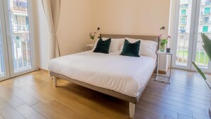 A bedroom with a bed, a nightstand, a window with curtains, and a view of buildings outside. - Musto Suites & Rooms (Naples)