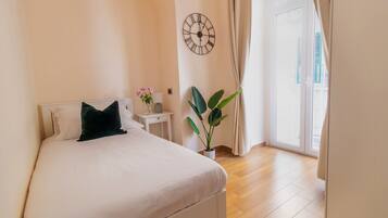 A bedroom with a bed, a nightstand, a potted plant, a wall clock, and a sliding glass door.