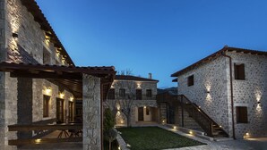A stone building with a covered patio and a small lawn. - Elafos Spa Hotel (Gortynia)