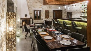 A restaurant with a long wooden table set for dining, stone walls, and a bar area. - Elafos Spa Hotel (Gortynia)