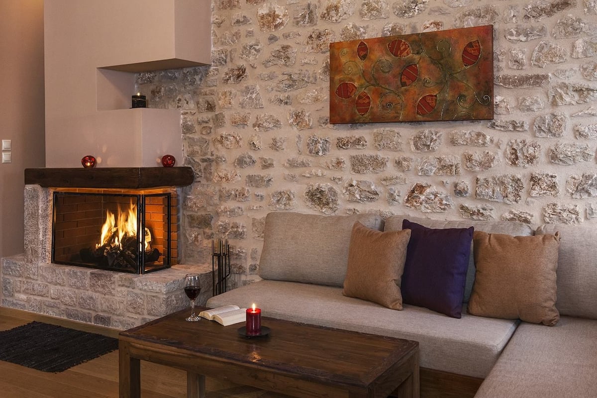 Ein gemütliches Wohnzimmer mit Steinwand, Kamin, einer Couch mit Kissen und einem Couchtisch mit Kerze.