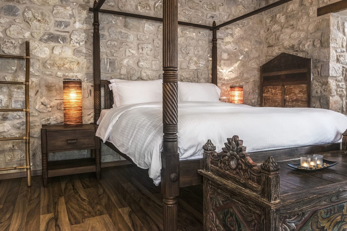 Ein Bett mit Himmelbett in einem Zimmer mit Steinwänden, Holzboden und einem geschnitzten Holztisch.