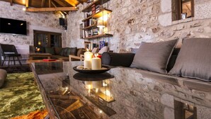 A modern living room with a stone wall, a glass coffee table with candles, and a cozy seating area. - Elafos Spa Hotel (Gortynia)