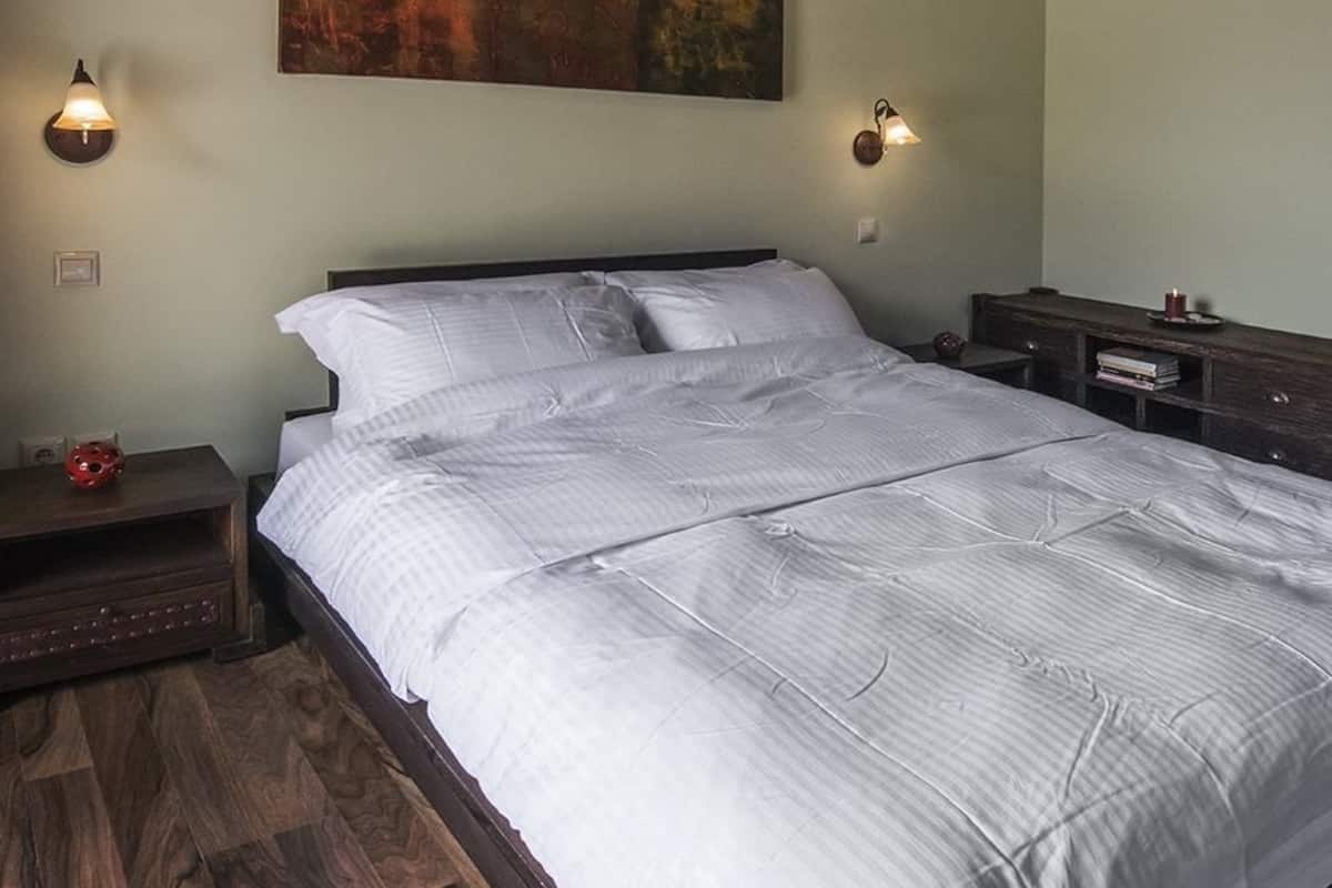 Ein Schlafzimmer mit einem großen Bett, einem Holzkopfstück, Holzboden, einem Bild an der Wand und zwei Nachttischlampen.