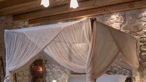 A bed with a canopy, wooden headboard, bedside tables, and a small table with a decorative item. - Elafos Spa Hotel (Gortynia)