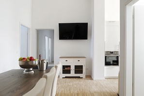 A modern kitchen with a wooden dining table, a bowl of fruit, a small cabinet, and a built-in oven.