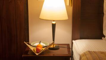 A hotel room with a wooden nightstand, a lamp, a basket with fruits, and a bed with a striped blanket.