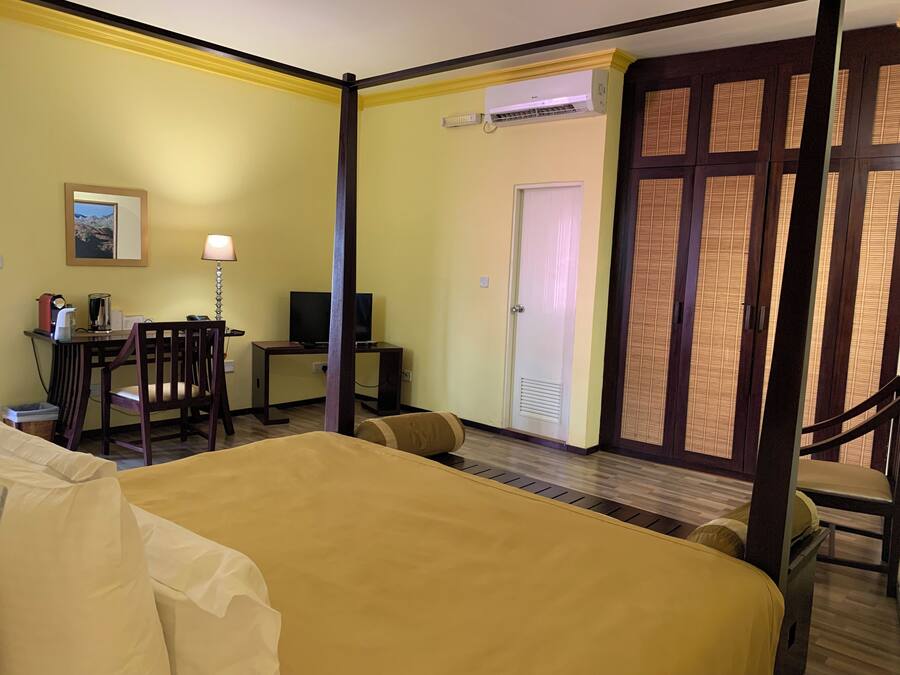 A hotel room with a bed, a desk with a chair, a television, and a door with a window.
