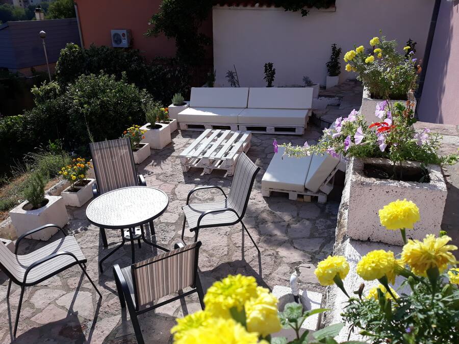 Un patio al aire libre con suelo de piedra, muebles blancos y plantas en macetas.