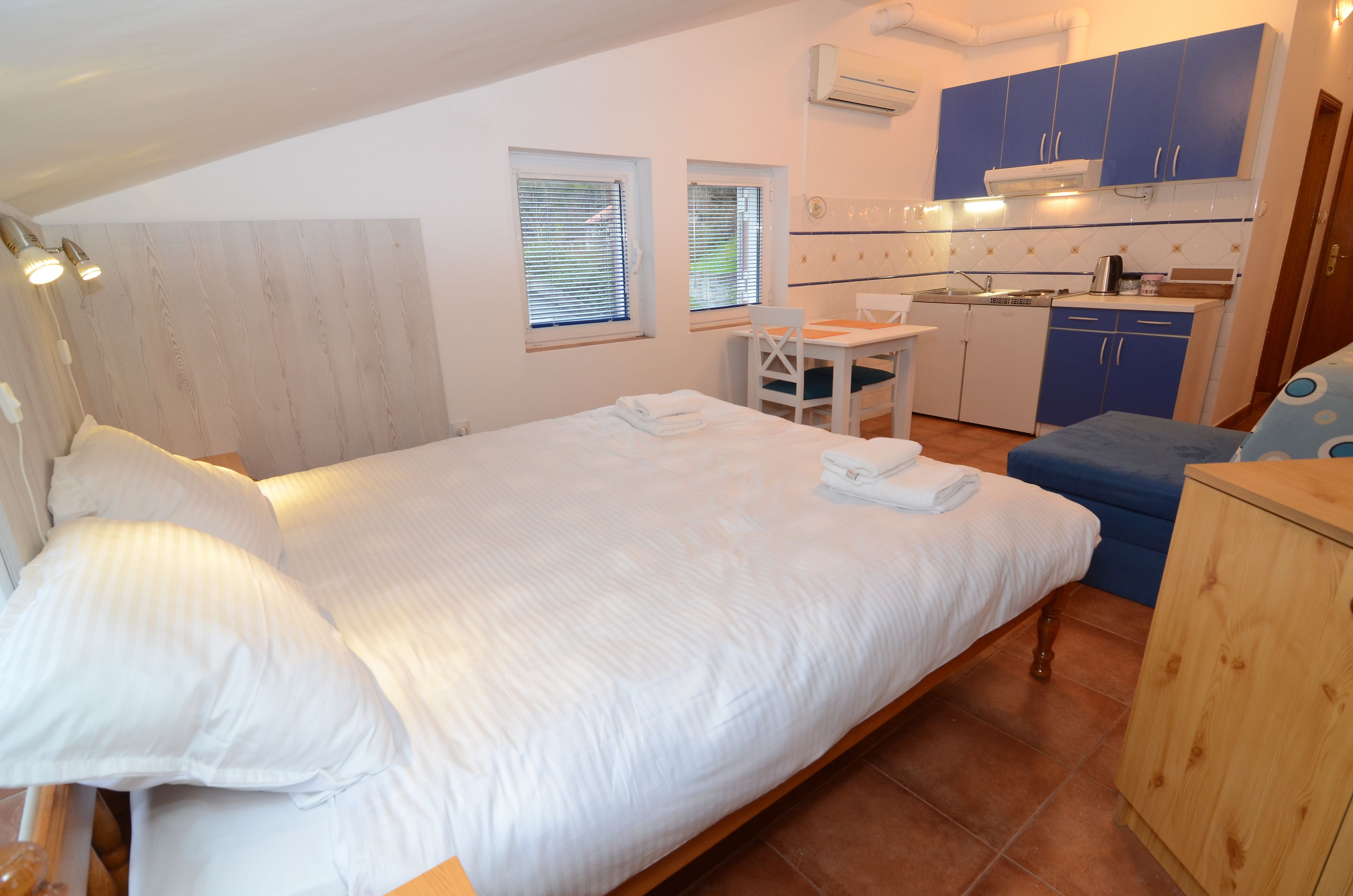 A bedroom with a bed, bedside table, and a small kitchenette with blue cabinets.