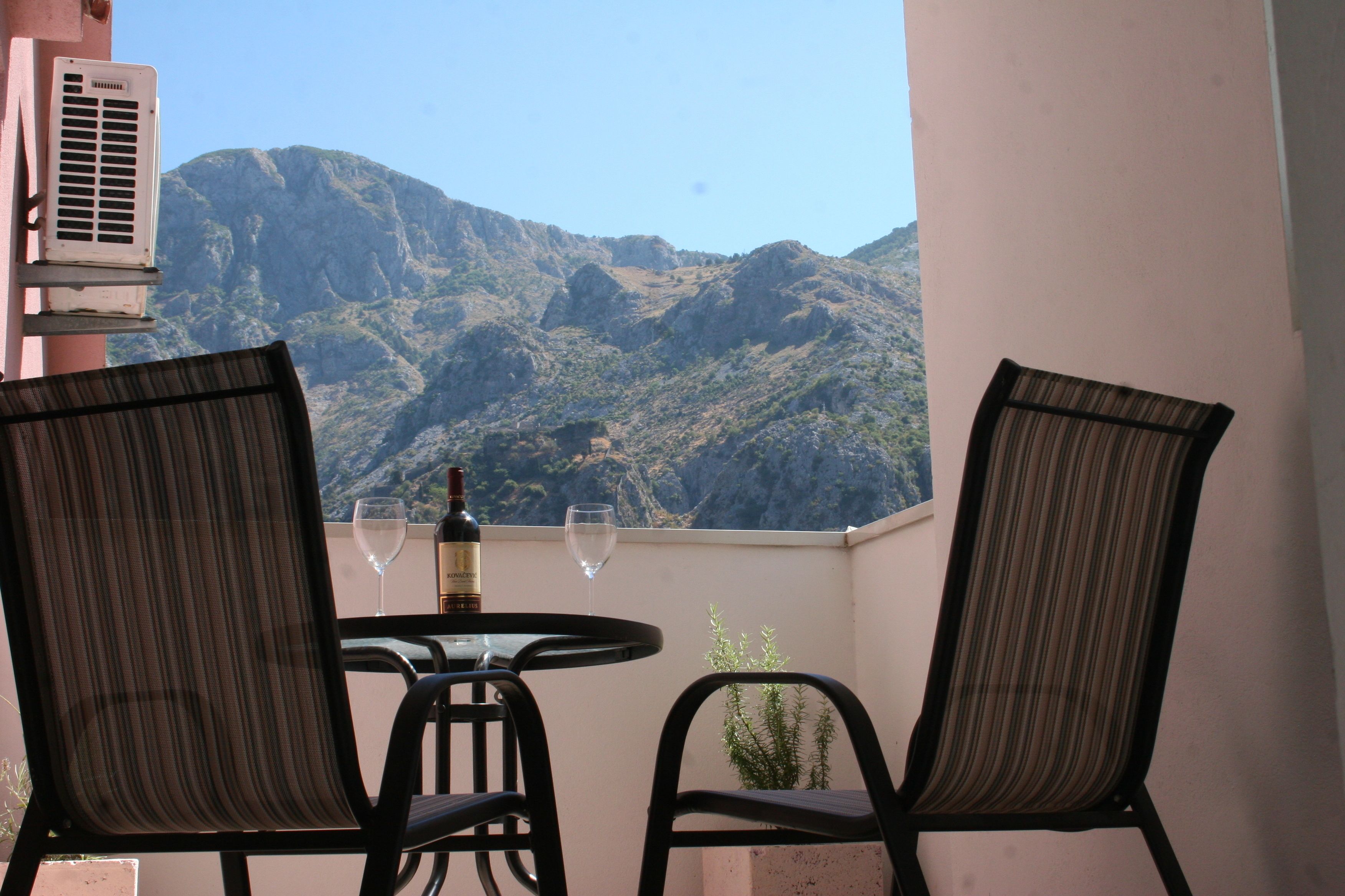 A balcony with two chairs, a table, and a bottle of wine, overlooking a mountainous landscape.