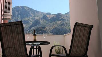 A balcony with two chairs, a table, and a bottle of wine, overlooking a mountainous landscape.