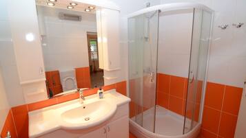 A bathroom with a white sink, a glass shower enclosure, and orange-tiled walls.