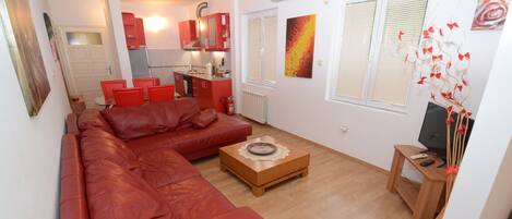 A living room with a red leather sofa, a wooden coffee table, and a TV on a wooden stand.
