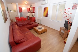A living room with a red leather sofa, a wooden coffee table, and a TV on a wooden stand. - Maritimo Apartments (Kotor)