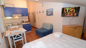 A compact hotel room with a kitchenette, a bed, a small seating area, and a television.