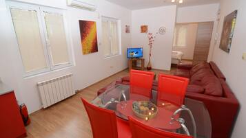 A modern living room with a glass dining table, red chairs, a red sofa, and a television.