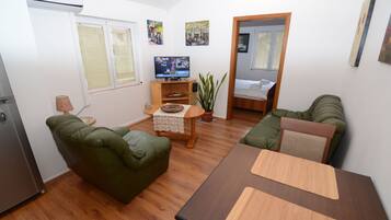 Un espacio habitable compacto con sofá, mesa de comedor, televisor y una planta en maceta.