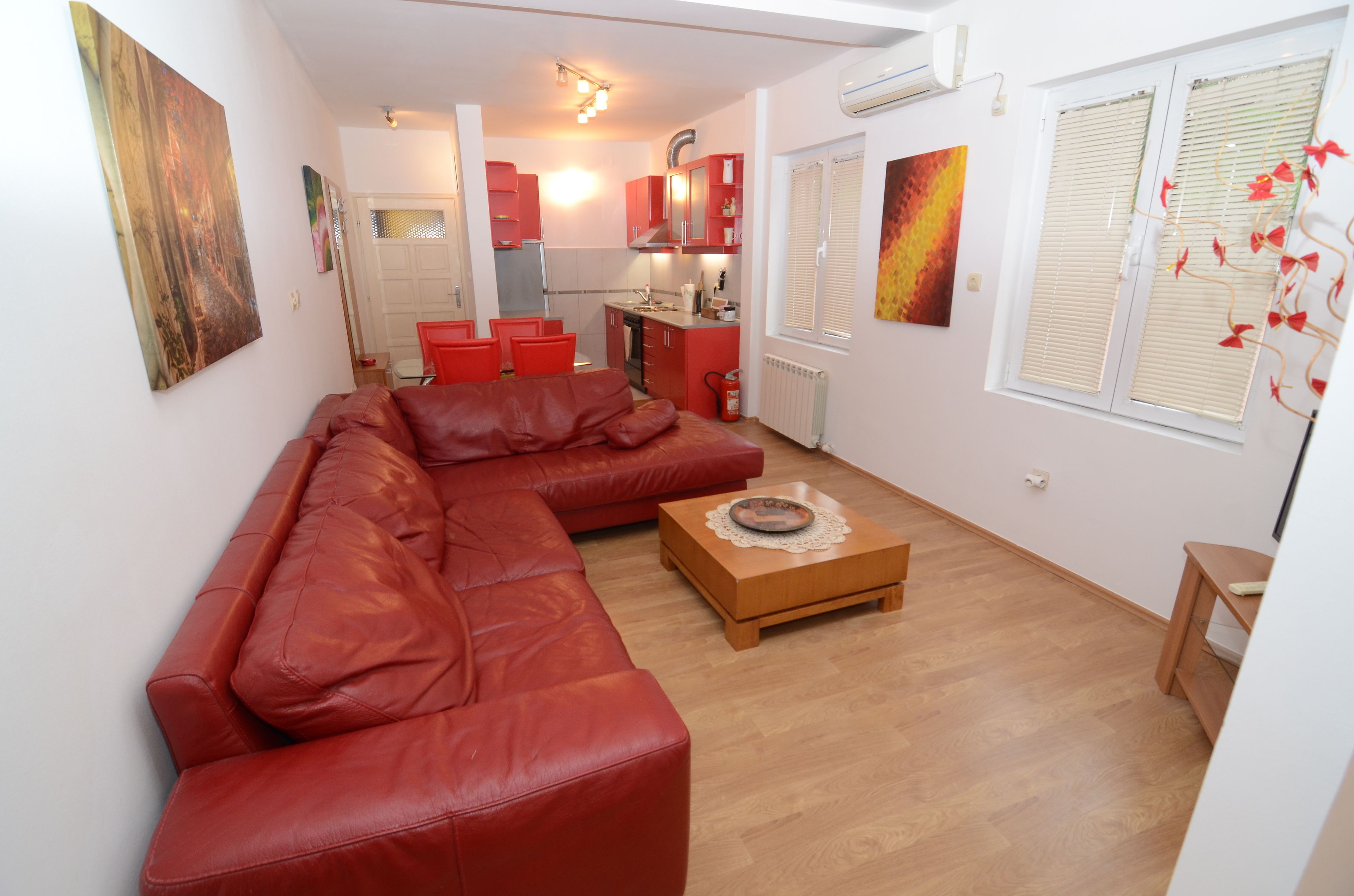 Ein Wohnzimmer mit einem roten Sofa, einem Holztisch und einer Küche im Hintergrund.