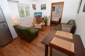A compact living space with a green sofa, a wooden dining table, a small TV on a wooden stand, and a potted plant. - Maritimo Apartments (Kotor)