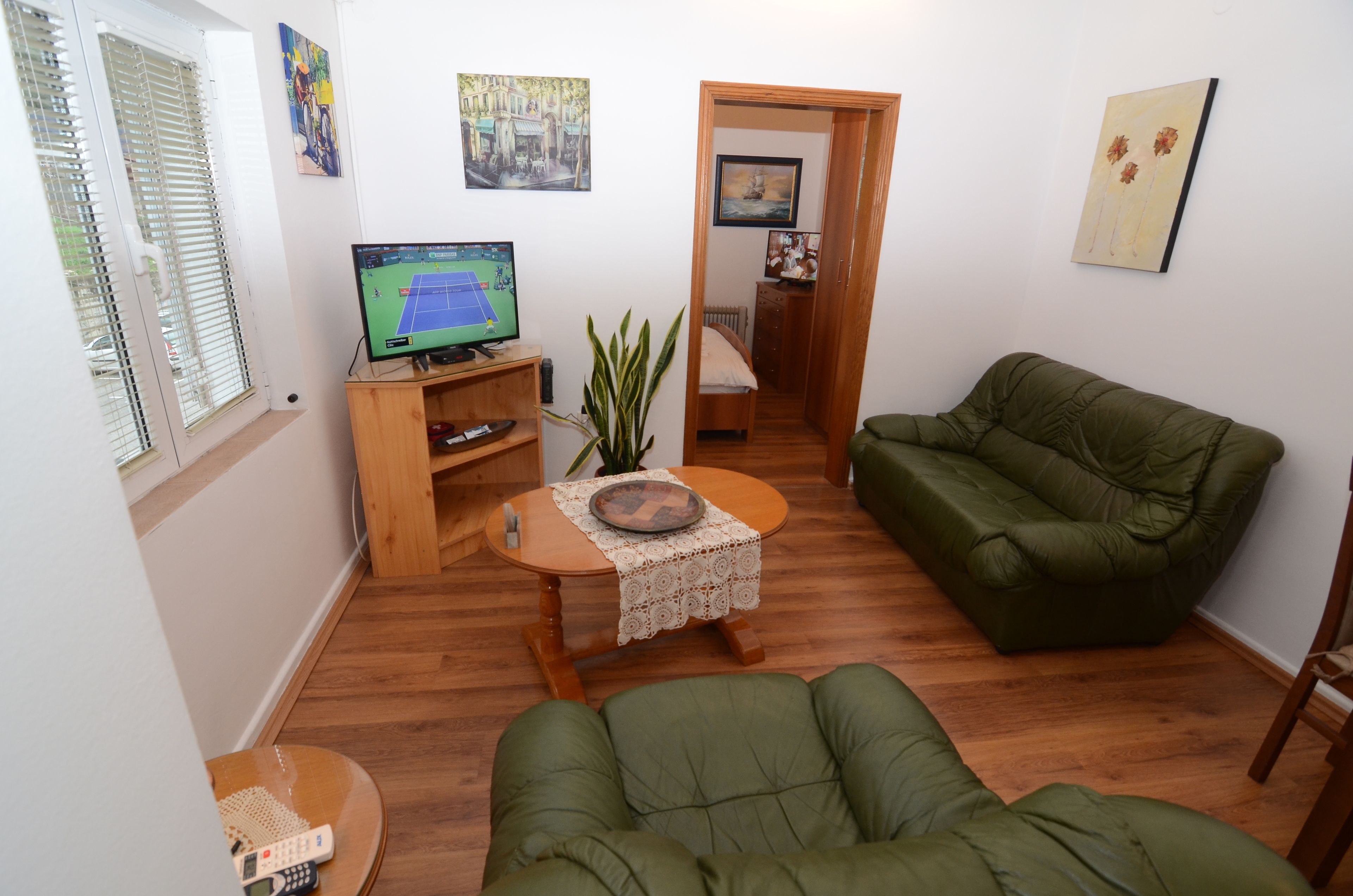 A cozy living room with a green sofa, a wooden coffee table, and a television displaying a tennis game.