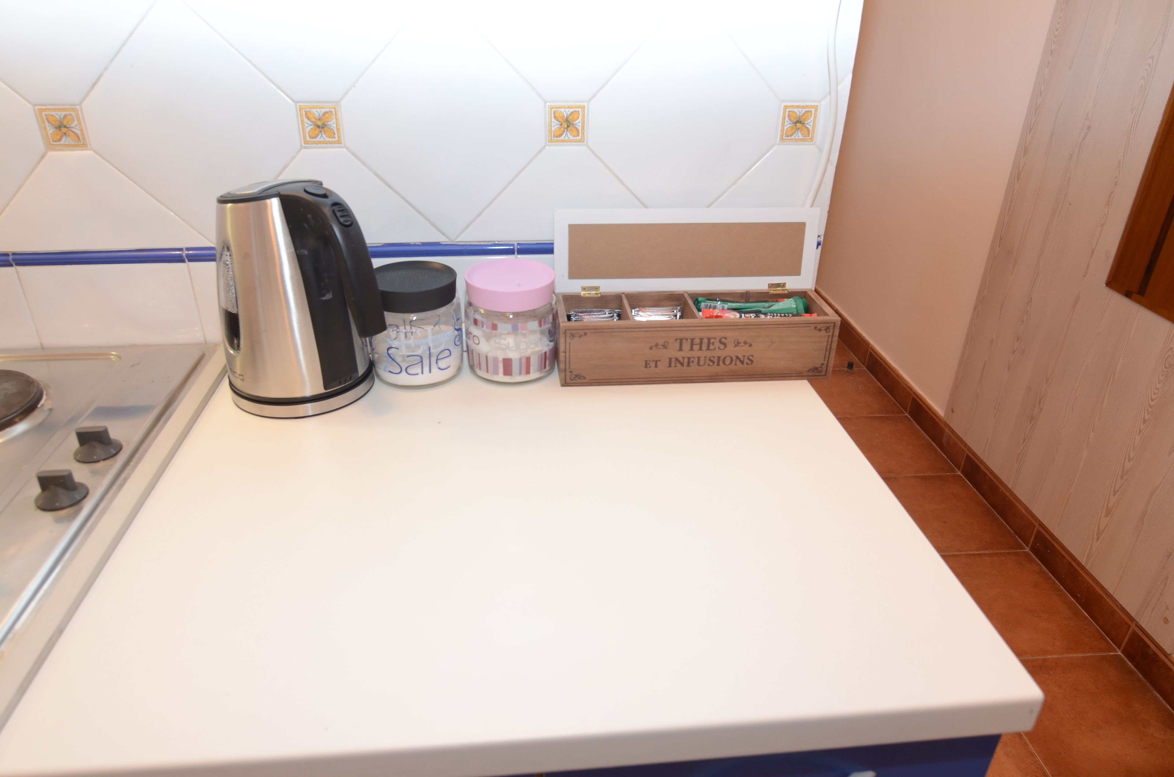 Una encimera de cocina con un hervidor, un tarro y una caja de madera con la etiqueta 'THES ET INFUSIONS'.