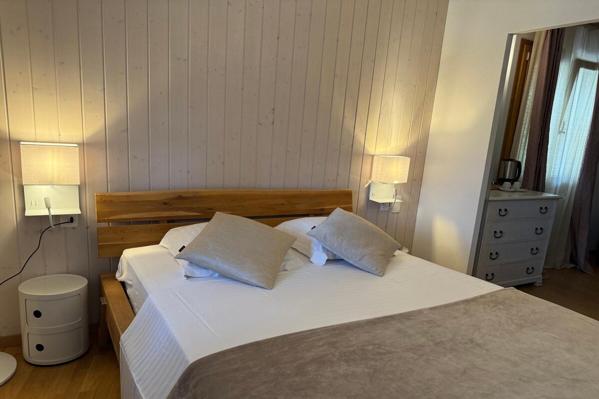 Un lit bien fait, avec des oreillers, une tête de lit en bois, des lampes de chevet, une petite table de chevet et une commode avec des tiroirs.
