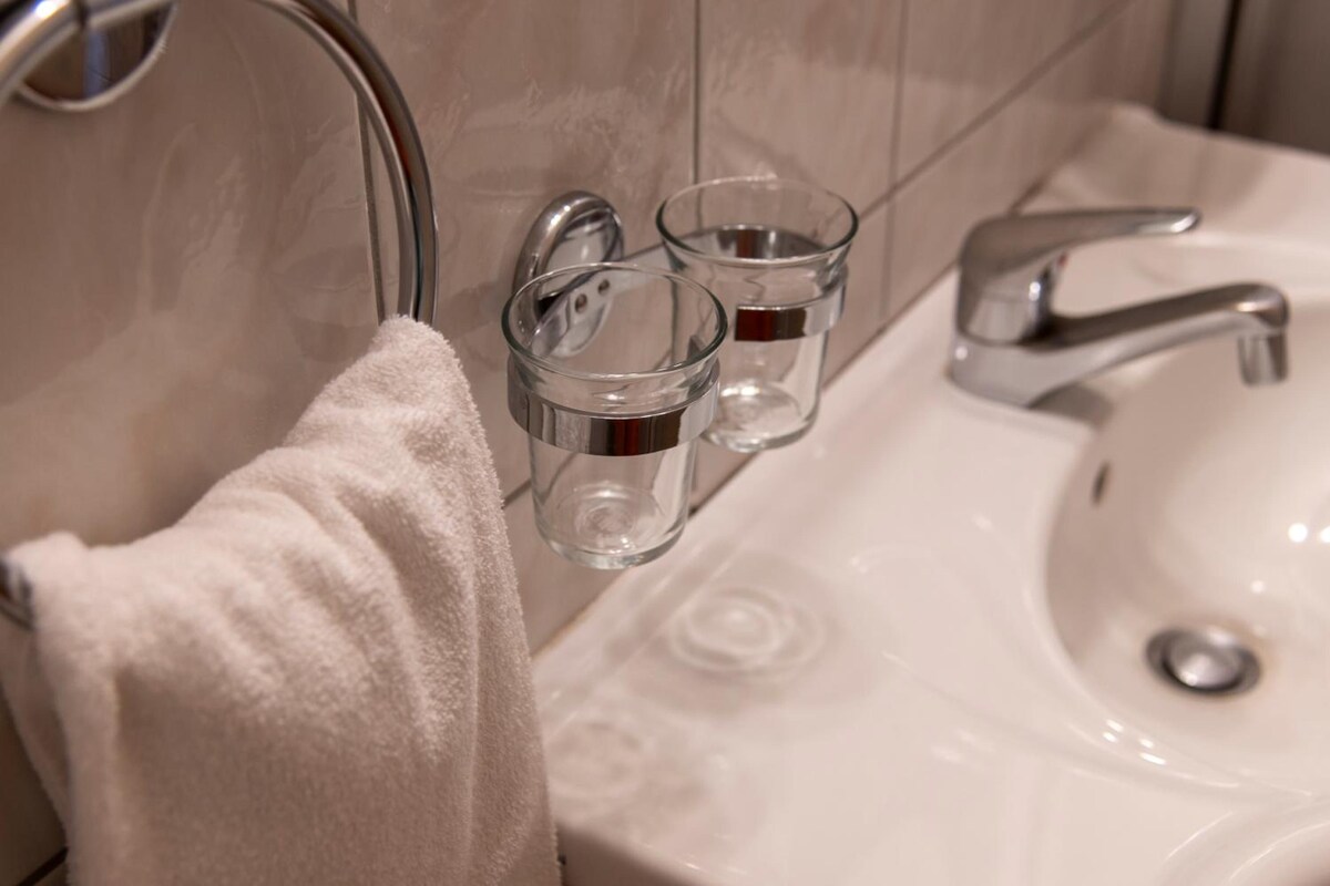 Une salle de bain avec un lavabo blanc, une serviette suspendue à un porte-serviettes et deux petits récipients en verre fixés au mur.