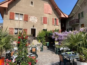 A building with a sign reading "CAFÉ & PLACE" and outdoor seating with tables and chairs. - Hotel de la place (Corsier-sur-Vevey)