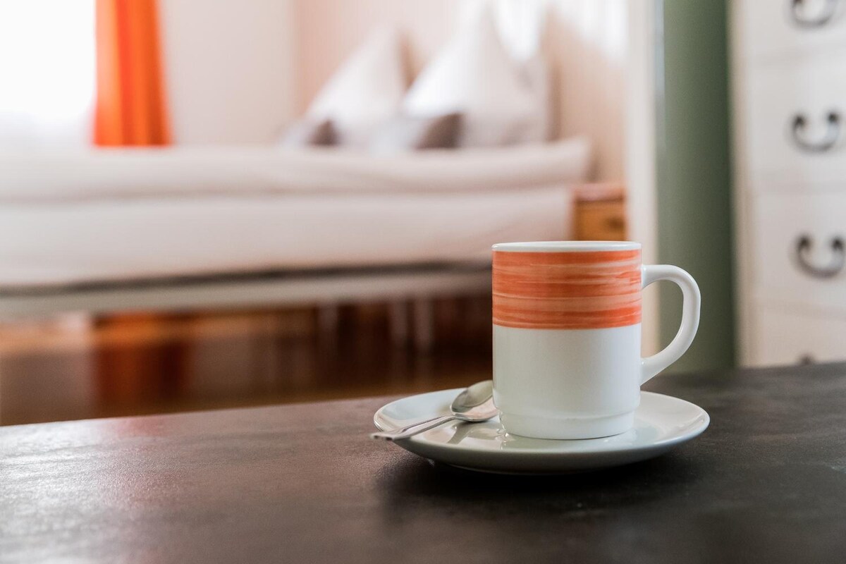 A white mug with orange stripes on a saucer, accompanied by a spoon, on a table.