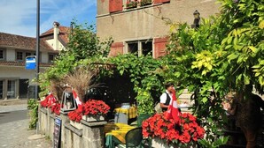 Ein Café mit Außenbestuhlung, roten Blumen und einem Schild.