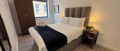 Une chambre à coucher comprenant un lit, une table de chevet, une lampe, une fenêtre, une armoire et une porte.