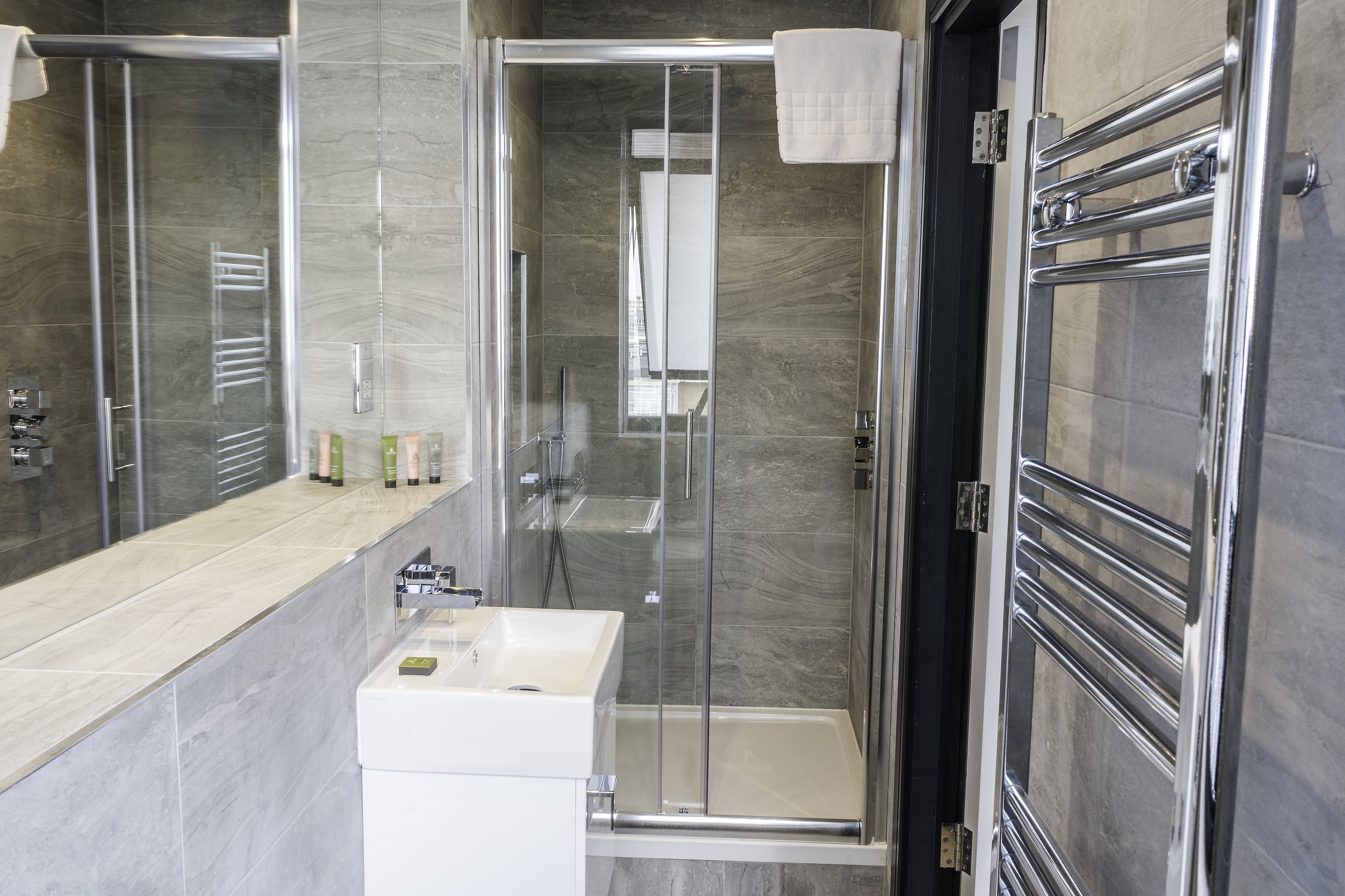 A modern bathroom with a glass-enclosed shower, a white sink, and a mirror.