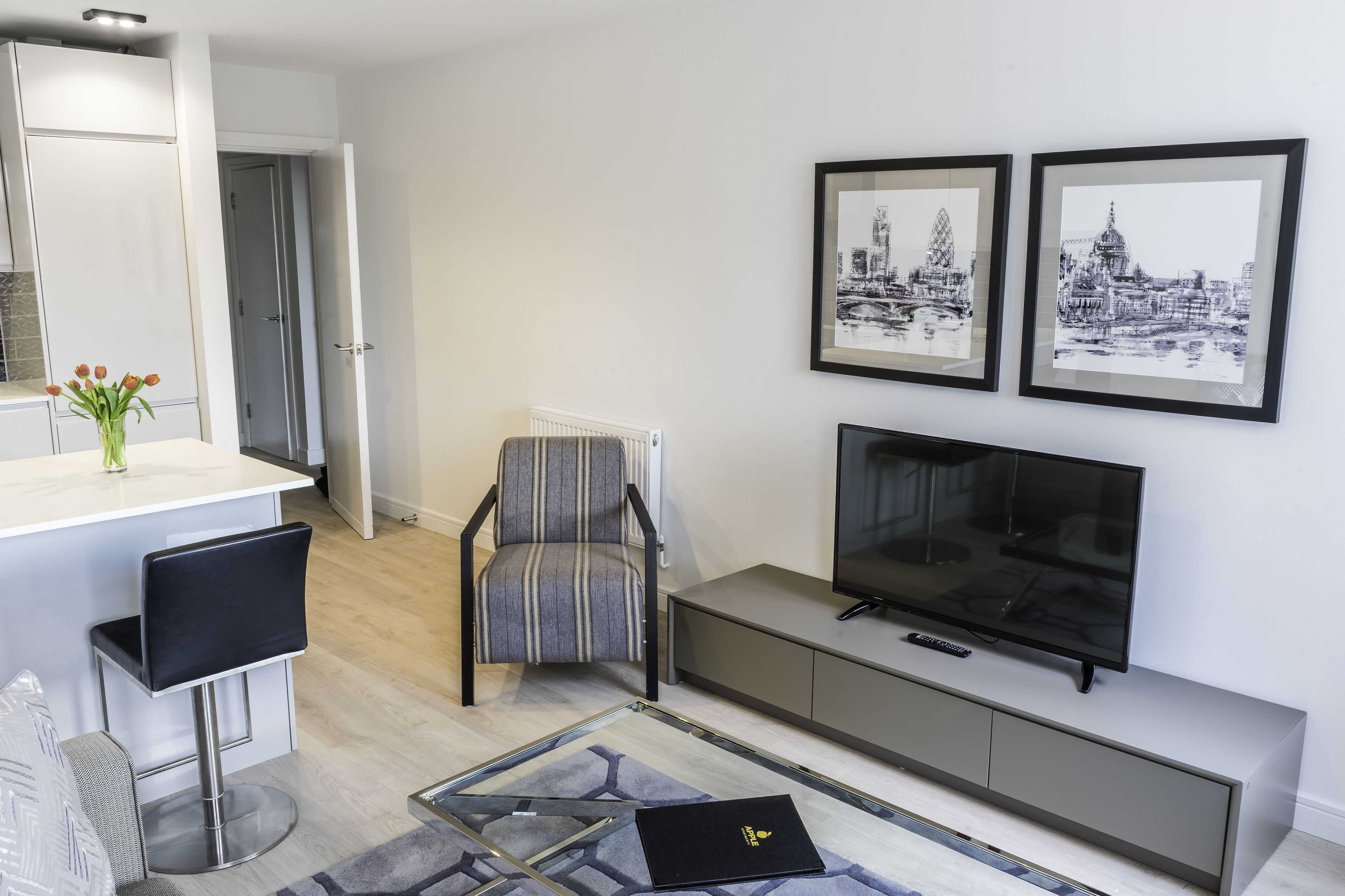 A modern living room with a TV, framed cityscape pictures, a striped chair, and a small bar area.
