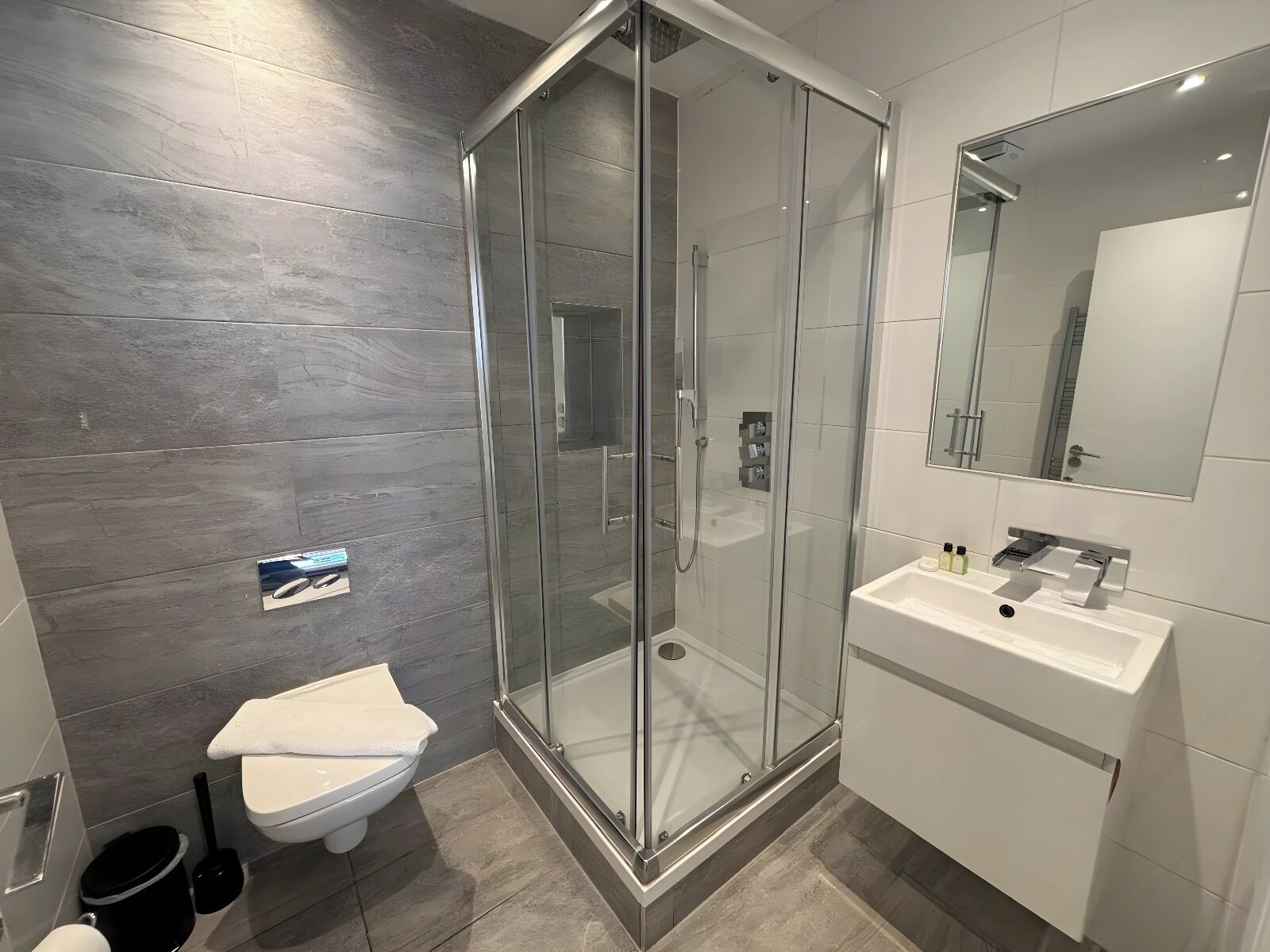 A modern bathroom with a glass-enclosed shower, a white sink, and a toilet.