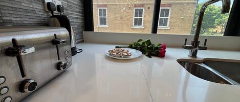 A modern kitchen with a stainless steel toaster, a sink, and a window offering a view of a brick building.