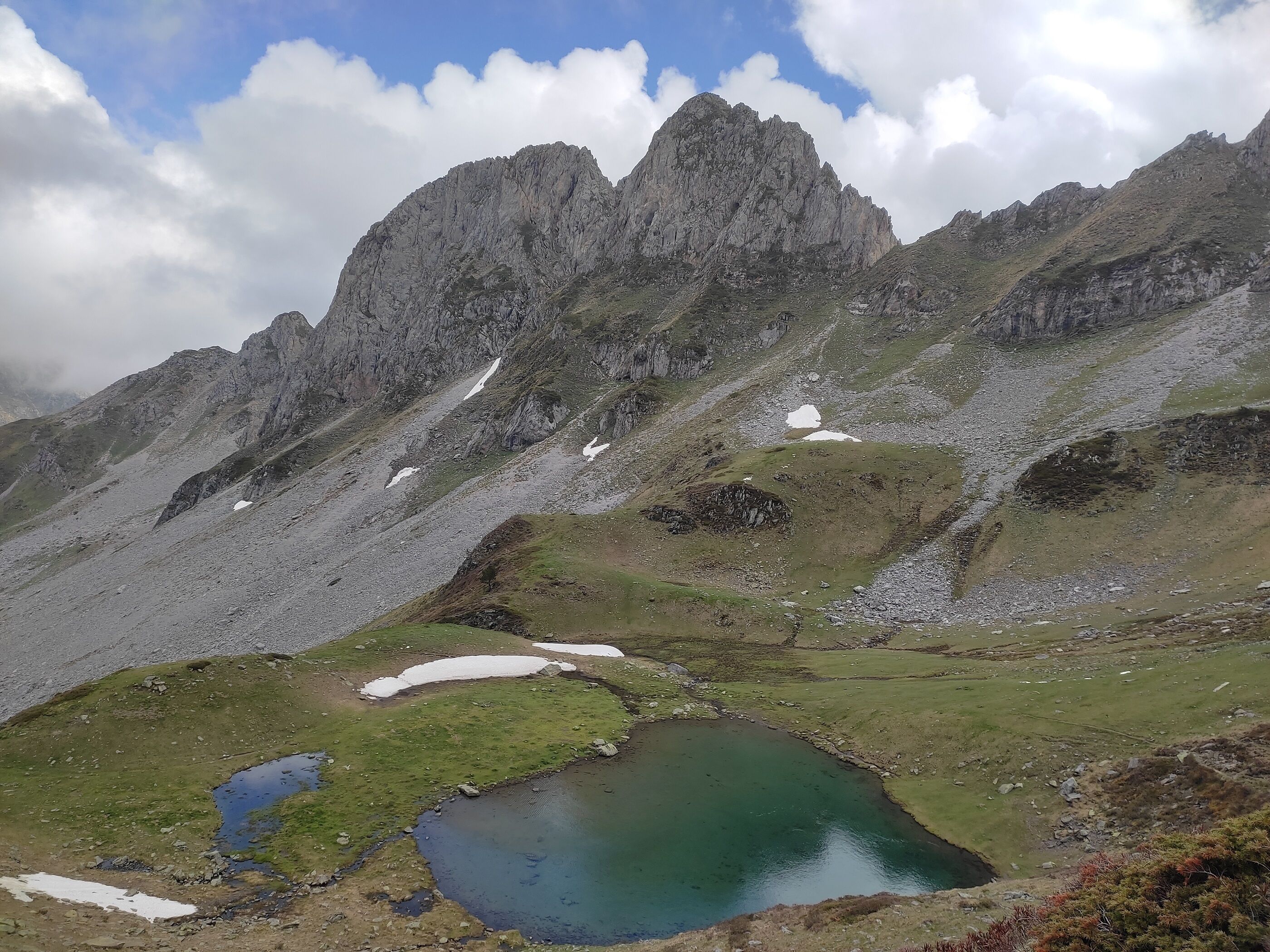 Un paysage montagneux avec un petit lac et quelques zones enneigées.