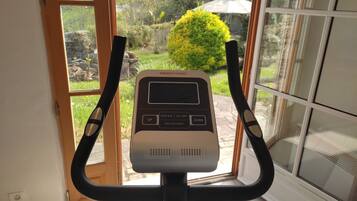 Una bicicleta estática con pantalla digital, ubicada cerca de una ventana con vistas a un jardín.