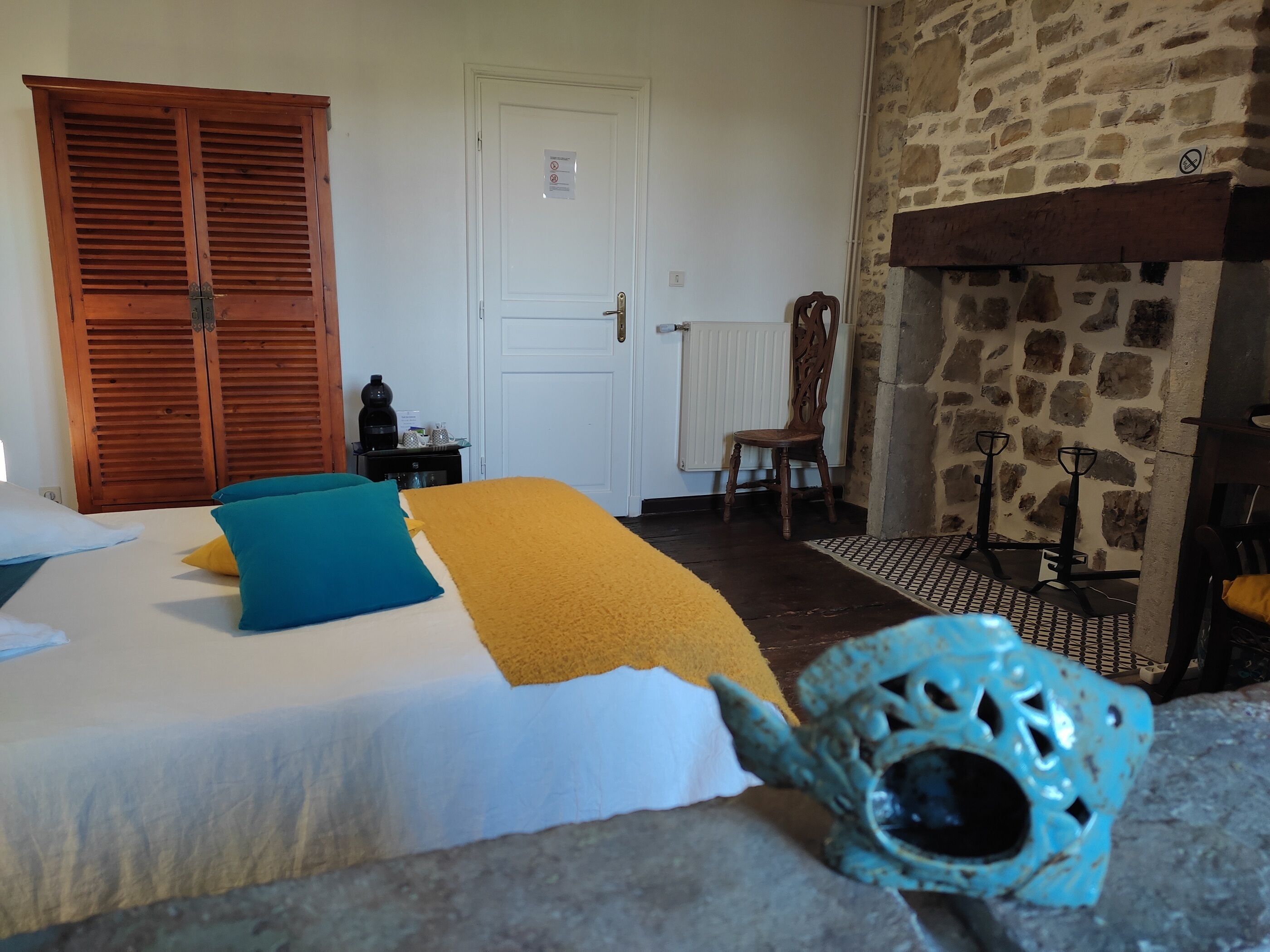 A room with a bed, wooden shutters, a stone wall, a radiator, and a chair.
